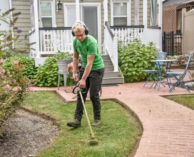 A man trimming weeds on a lawn using a weed trimmer